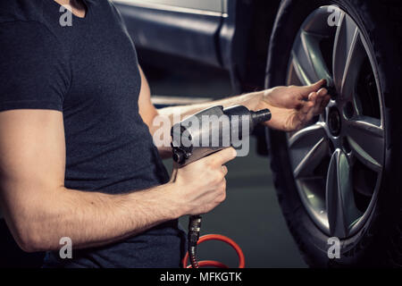 Männliche Automechaniker mit Reifen und Schraubenschlüssel, Schrauben Rad in der Werkstatt Stockfoto