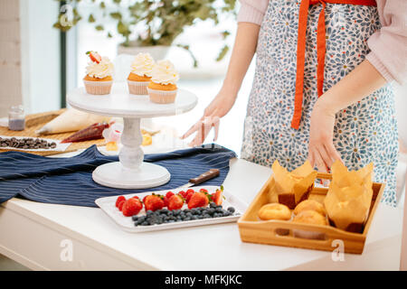 7/8-Ansicht von Frau Baker dekorieren Cupcakes, halten sich an den Händen auf dem Tisch Stockfoto