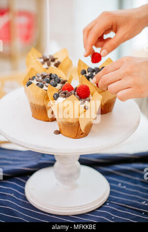 Nahaufnahme von Frau Hände bereiten leckere Cupcakes mit cremigen Belag mit Beeren auf den Tisch dekoriert Stockfoto