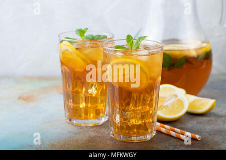 Traditionelle Eistee mit Zitrone, Minze und Eis in hohe Gläser. Zwei Gläser mit kühlen Sommer Drink auf alten rostigen Hintergrund. Stockfoto