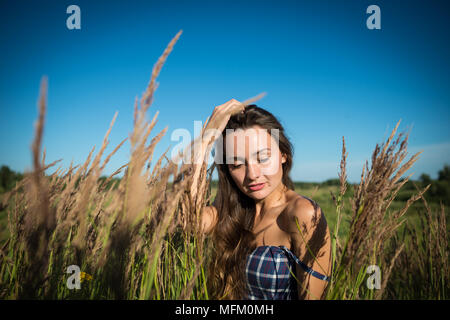 Junge hübsche Frau versteckt in einem Feld von Gras in die Landschaft. Schöne Mädchen genießt die sonnigen Tag auf dem Hintergrund der Natur. Stockfoto