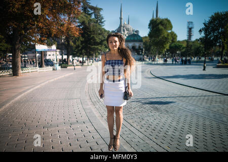 Junge lächelnde Frau springt bei Square auf dem Hintergrund der Moschee und Bäume im Sommer sonnigen Tag. Hübsches Mädchen mit langen Haaren genießt Urlaub in Istanbul Stockfoto