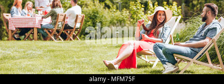 Glückliche Frau entspannen mit einem Freund auf Sonnenliegen während der sonnigen Tag im Sommer Stockfoto