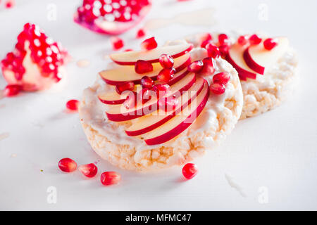 Knäckebrot gesunden Snack mit Apfelscheiben, weiche Hüttenkäse, Vanille, Honig, Granatapfel Samen. Einfaches Frühstück, das auf einen weißen Hintergrund mit Stockfoto