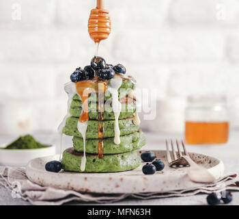 Grüne Pfannkuchen mit Matcha Tee, gekleidet, Blaubeeren, weiße Vanillesauce oder kondensierte Milch und Honig. Ideen und Rezepte für gesundes Frühstück mit superfood Zutaten. Stockfoto