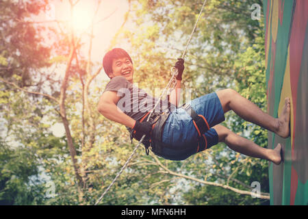 Asiatische jüngeren Mann hängen an Clip wandern Sicherungsseil und Lachen mit Glück emotion Stockfoto