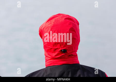 Person mit einem roten Haube aus hinter blickt auf das Meer Stockfoto