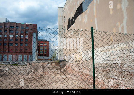 Entwicklung Website in der urbanen Landschaft. Gebäude aus rotem Ziegel, grauer Himmel, grünen Zaun Surround gelöscht, zukünftige Baustelle Stockfoto