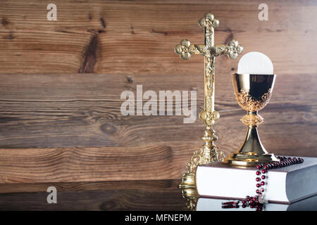 Die erste heilige Kommunion. Das Kreuz, Bibel, Rosenkranz und goldenen Kelch auf braunem Hintergrund. Stockfoto