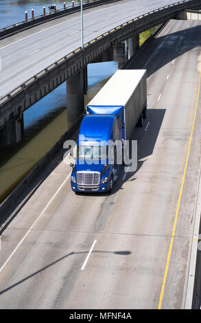 Big Rig blau American Semi Truck Transport von kommerziellen Ladung im abgedeckten Auflieger mit Spoiler unter Drehen überführung Straße Kreuzung entlang der Stockfoto