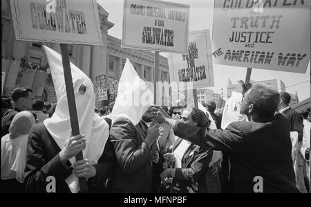 Ku Klux Klan Mitglieder Unterstützung von Barry Goldwater's Campaign für die präsidentschaftskandidatur an der Republican National Convention, San Francisco, Kalifornien, eine afroamerikanische Mann schiebt Zeichen zurück: 12. Juli 1964. Fotograf: Warren K Leffler. Stockfoto