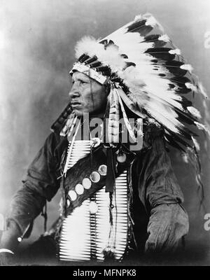 Roter Vogel, Sioux Indianer, Brustbild, Sitz, nach links, das Tragen von gefiederten Kopfschmuck, c 1908. Foto von John A. Johnson Stockfoto