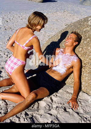 Seite Profil einer jungen Frau applaying Sonnencreme auf der einen jungen Mann Brust Ref: CRB421 10034 035 obligatorische Credit: Sven Arnstein/Photoshot Stockfoto