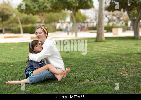 Zwei Schwestern, die das Sitzen einander zu lieben. In einem Park in der Stadt San Vicente del Raspeig in der Provinz Alicante in Spanien. Stockfoto