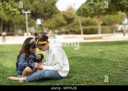 Schwestern ein Mobiltelefon in einem Park. In einem Park in der Stadt San Vicente del Raspeig in der Provinz Alicante in Spanien gedreht. Stockfoto