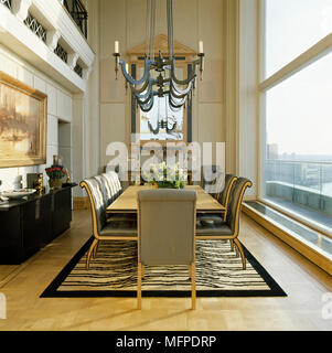 Palastartigen Speisesaal mit großen Fenster, Spiegel, und eine Kerze Kronleuchter über einen Holztisch mit gepolsterten Stühlen. Stockfoto