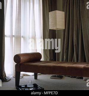 Ein modernes Wohnzimmer detail ein braunes Leder Sitz vor eine moderne Stehleuchte mit einem großen Fenster mit einer transparenten Folie abgedeckt. Stockfoto