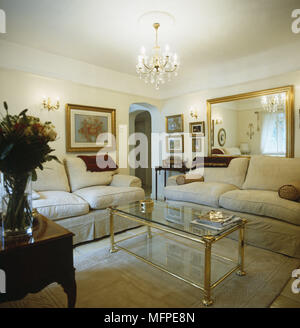 Ein traditionelles Wohnzimmer mit einem Kronleuchter ausgesetzt über einen Couchtisch aus Glas umgeben von beige Sofas mit einem gold gerahmten Spiegel in der backgroun Stockfoto