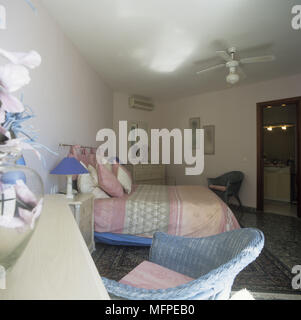 Schlafzimmer mit Ventilator über ein Bett mit rosa und blau Bettwäsche und einem blauen Korbstuhl im Vordergrund. Stockfoto