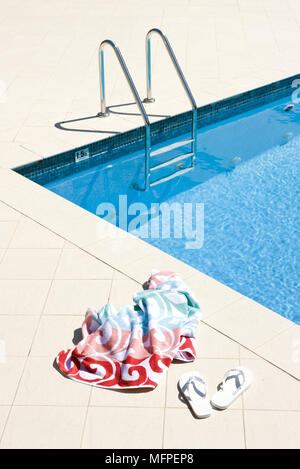 Strandtuch und Flip Flops neben Schwimmbad Stockfoto