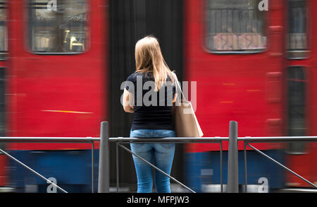 Junge Frau in schwarzen T-Shirt und Jeans an der Haltestelle und Stadtverkehr in motion blur warten Stockfoto