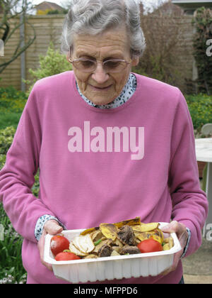 Ältere Frau unter recycling Küchenabfälle zur Startseite Komposter bin (in ökologischer Weise für natürliche Garten Laubdecke benutzt) Model Released Stockfoto