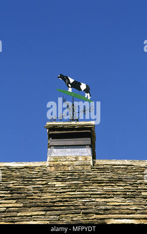 Barn rooftop with a metal cow weathervane against a clear, blue sky. Stockfoto