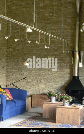 Wohnzimmer in einer umgebauten Scheune mit gefliestem Boden, Wände aus Stein, Holzofen, gepolsterten Sofas und Holz-Kaffeetischen und angehalten, Anschluss lig Stockfoto