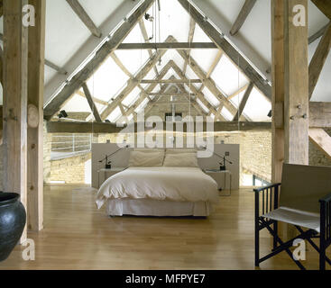 Schlafzimmer im Loft in einer umgebauten Scheune mit Holzfussboden, sichtbare Dachstühle, Director's Chair, und ein Doppelbett. Stockfoto