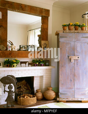 Land Wohnzimmer mit einem gemalten gemauerten Kamin, Holz Spiegel, rustikalen Schrank und Volkskunst. Stockfoto