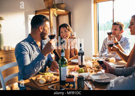 Gruppe von Freunden reden und Trinken am Esstisch zu Hause sitzen. Männer und Frauen Freunde Mahlzeit zu Hause zu genießen. Stockfoto