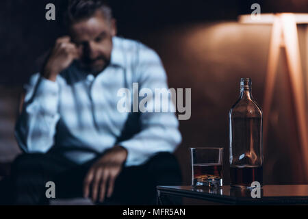 Betont man in einem dunklen Raum mit einer Flasche und Glas mit Alkohol sitzen Stockfoto