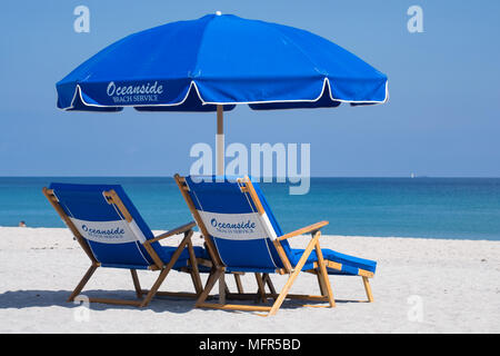 Entspannen Sie sich in Delray Beach, Florida auf dem Sand, unter einem Sonnenschirm, Liegestühle mit Blick auf das tiefblaue Meer. Stockfoto