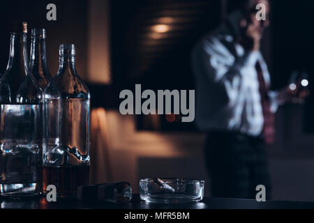 Flaschen Alkohol und Zigaretten auf einen Tisch mit einem Mann am Telefon zu sprechen im Hintergrund Stockfoto