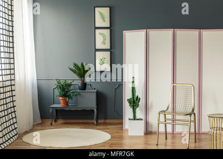 Elegantes Wohnzimmer Einrichtung mit Pflanzen auf schwarzen Schrank neben einem weißen und rosa mit gold Stuhl und Kaktus auf der Vorderseite Stockfoto
