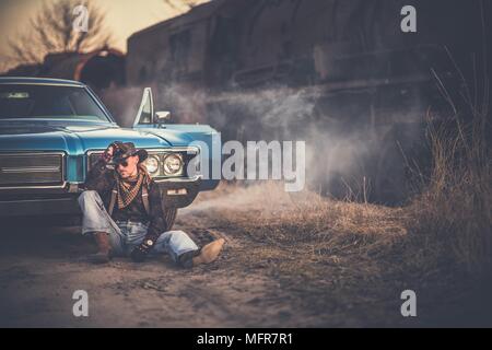 Die amerikanische Cowboy Geschichte. Kaukasische Männer tragen westliche Kleidung und Cowboyhut, sich einen Moment Zeit nehmen, Vor seinem American Classic Muscle Car. Ag Stockfoto