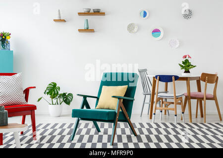 Gelbe Kissen auf grünen Sessel in bunten open space Interieur mit Stühle am Esstisch Stockfoto