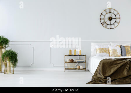 Industrielles Rackmontage mit goldenen Kerzen, großes Bett mit dekorativen Kissen und Wanduhr im Hotel Schlafzimmer Innenraum Stockfoto