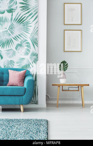 Blatt auf hölzernen Tisch gegen graue Wand mit Plakaten im Wohnzimmer Innenraum mit blauen Couch Stockfoto