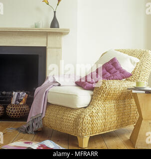 Landhausstil Korbstuhl mit Kissen und Decke neben einem Kamin Stockfoto