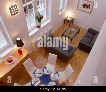 Überblick über eine moderne, offene Wohnraum mit Holzboden, Sofas und einem runden Esstisch aus Glas mit gepolsterten Stühlen. Stockfoto