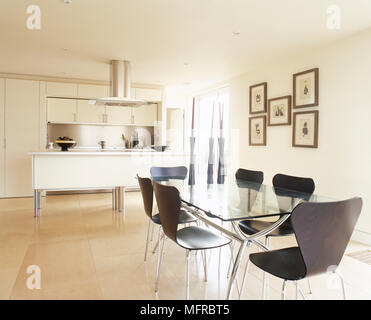 Küche und Essbereich mit einem Glas Tisch, Stühle aus Holz, Fliesen und zentrale Insel mit Edelstahl Haube. Stockfoto