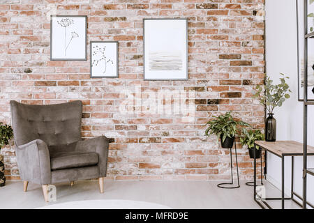 Wohnzimmer Einrichtung mit grauen Sessel, Pflanzen und Poster auf einem Red brick wall Stockfoto