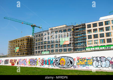 Blick auf den ursprünglichen Abschnitt der Berliner Mauer mit neuen Bürogebäude im Bau nach hinten an der East Side Gallery in Friedrichshain, Berlin, Deutschland. Stockfoto