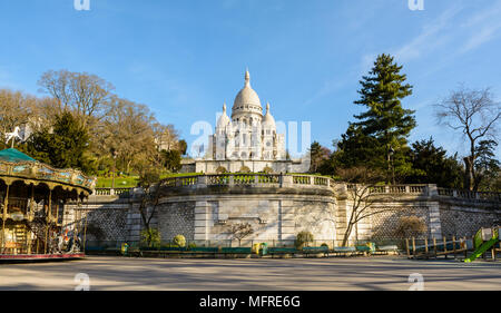 Panoramablick auf die Basilika des Heiligen Herzen von Paris von der Unterseite der Louise Michel Park, mit einem Karussell im Vordergrund im Frühjahr. Stockfoto