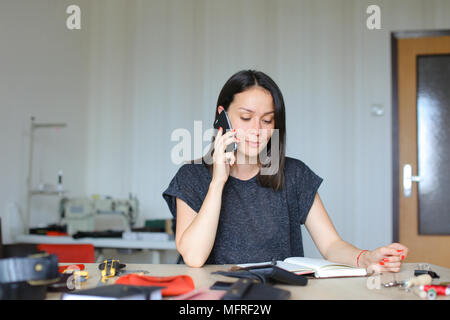 Weibliche Person sitzen an Leder Atelier und handmade Notebook und Mappen, Reden von Smartphone Stockfoto