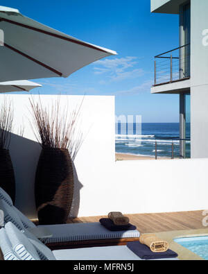 Ein Detail von einem modernen Haus mit einem Swimming Pool Sonnenliegen mit Sonnenschirmen weiß getünchten Wänden Stockfoto