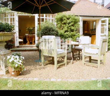 Ein Land Haus Garten mit einem Geschotterten Terrasse mit Tisch und Stühlen Sonnenschirm Blumen in Töpfe Stockfoto