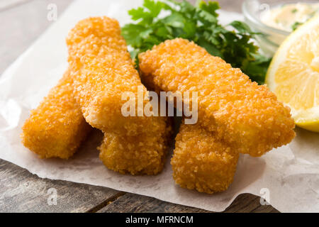 Knusprig gebratenen Fischstäbchen mit Zitrone und Soße auf Holz- Hintergrund Stockfoto