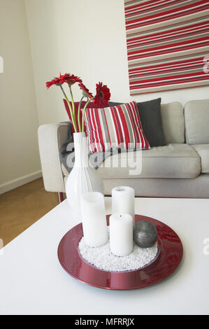 White Couchtisch mit Teller von Kerzen und Vase mit Blumen vor dem Sofa mit rot gestreiften Kissen Stockfoto